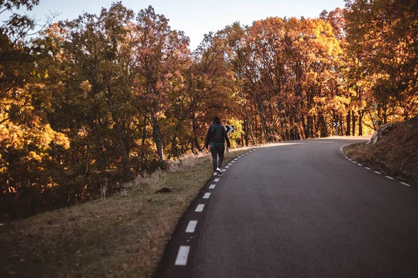 Strada autunnale in montagna. Giovane donna a piedi lungo la strada asfaltata in faggio colorato autunno e bosco di querce — Foto Stock