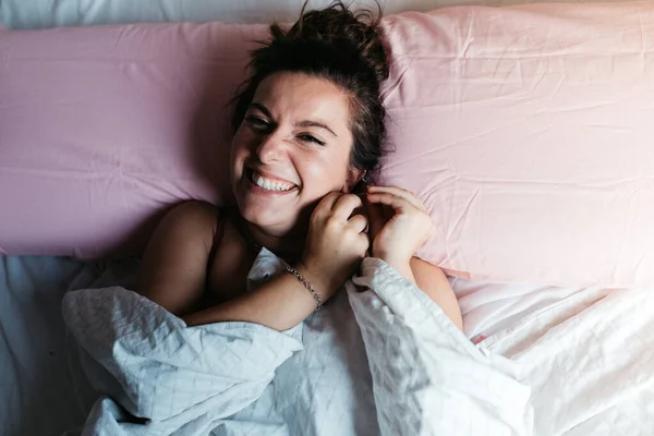 ผู้หญิงหัวเราะสัมผัสหูของเธอ พยายามที่จะหลับนอนลงบนเตียง ยิ้มอย่างมีความสุขและผมยาวสวย แนวคิดไลฟ์สไตล์ ท็อปวิว . — ภาพถ่ายสต็อก