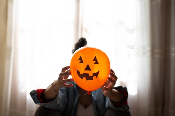 Bruxa segurando um balão de abóbora com as mãos e cobrindo o rosto. Uma jovem que celebra o Halloween. Balões de festa de hélio . — Fotografia de Stock