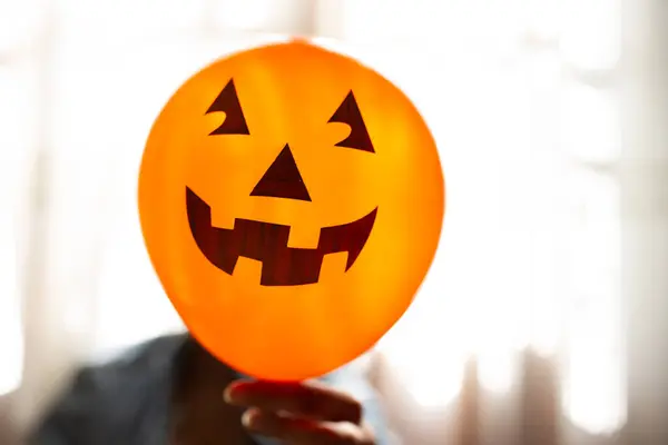Bruxa segurando um balão de abóbora com a mão e cobrindo o rosto. Uma jovem que celebra o Halloween. Balões de festa de hélio . — Fotografia de Stock