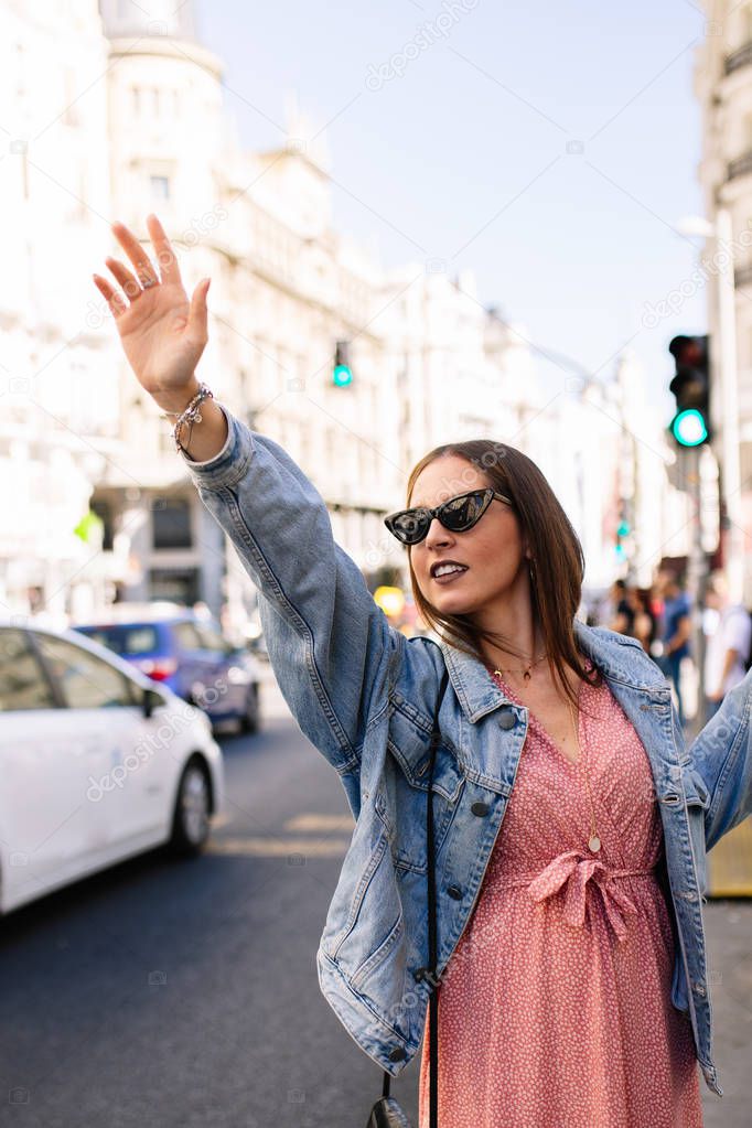 Young brunette woman asking for a taxi raising her arms in Madri