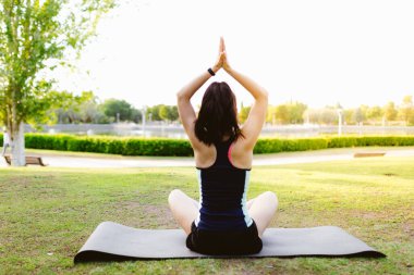 Parktaki genç esmer kadın yoga yapıyor ve paspasın üzerinde geriniyor.