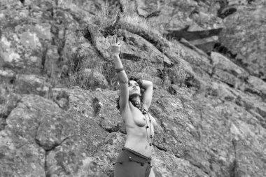 kayaların önünde tahta sopa ile genç Kafkas güzel çıplak Amazon kadın duruyor. siyah ve beyaz.