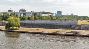 BERLİN, GERMANY - 13 HAZİRAN 2018: İnsanlar Mitte 'nin sıcak bir yaz gününde Spree Nehri gezinti alanında dinlenirken, arkada Reichstag ve hükümet binaları bulunuyor.