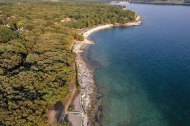 Hırvatistan 'ın Istria kentindeki Istria kentindeki ormanlık Lanterna yarımadası tatil beldesinin hava gün batımı drone görüntüsü, etrafı oteller ve eğlence tesisleriyle çevrili Adriyatik sularıyla çevrili. Arkaplanda Cervar-Porat