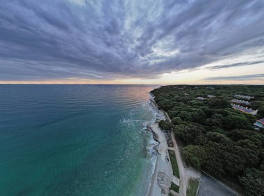 Hırvatistan 'ın Istria kentindeki altın saat gün batımında kıyı şeridi, turkuaz sular ve orman manzarasını gösteren nefes kesici Lanterna yarımadasının insansız hava aracı panoraması.