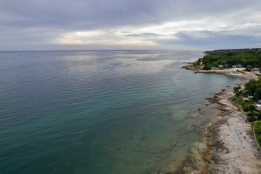 Hırvatistan 'ın Istria kentindeki altın saat batımında, kamp, kıyı şeridi, turkuaz sular ve orman manzarasını gösteren Lanterna yarımadasının nefes kesici hava aracı görüntüsü.