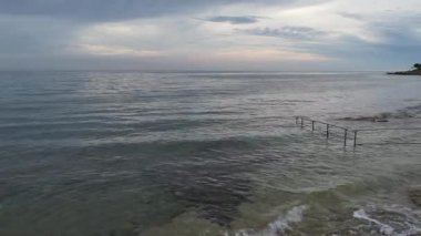 Bulutlu bir akşam gökyüzü altında kayalık kıyıları ve sakin suyu olan huzurlu deniz manzarası seyahat, rahatlama ve doğa temaları için mükemmeldir..