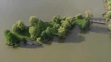 Nagykanizsa yakınlarındaki huzurlu Macaristan kırsalında sakin bir kayık gölü üzerinde hava aracı manzarası. Bereketli yeşil bitki örtüsü, ağlayan söğütler cennet gibi deniz manzarası yaratır..