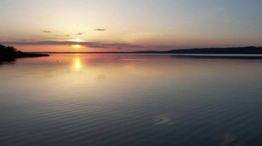 Canlı turuncu ve sarı gökyüzü sakin su yüzeyine yansıyan Balaton Gölü üzerinde nefes kesici bir gün batımı. Mükemmel altın saat ışıklandırması çarpıcı Macar göl manzarası yaratır..
