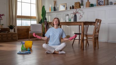 Genç bayan odayı temizler ve meditasyon pozuna oturur, lastik eldivenler.