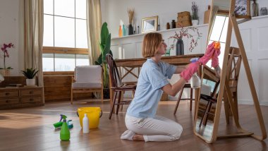 Kadın ya da hizmetçi aynayı evde lastik eldivenlerle yıkıyor, temizlik yapıyor.