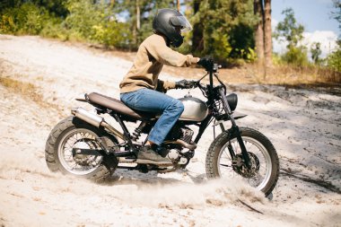 Rahat sweetshirt ve eylem eğlence için kum zemin üzerine yeşil orman ise motosiklet sürme kot giyen genç, güçlü ve yakışıklı adam