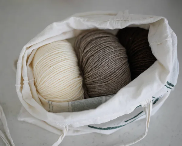 Traditional warm wool pastel yarns for home knitting in a cotton eco bag on a grey stone background.