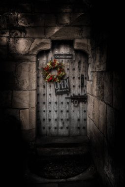 York, İngiltere, 12 Aralık 2018: Asma kilitli, renkli bir Noel süsü ve sizi içeri davet eden bir tabela ile ürpertici eski güçlü ahşap kapı.