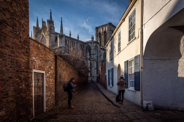 York, Engeland, 13 december 2018: mensen die Foto's maken in een geplaveide bakstenen straat die leidt naar de prachtige kathedraal van York Minster, met smalle rode bakstenen muren aan beide zijden. — Stockfoto
