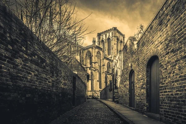 YORK, ENGLAND, DECEMBER 13, 2018: cobbled brick street that leads to the magnificent York Minster Cathedral, with narrow red brick walls at both sides. — Stock Photo, Image