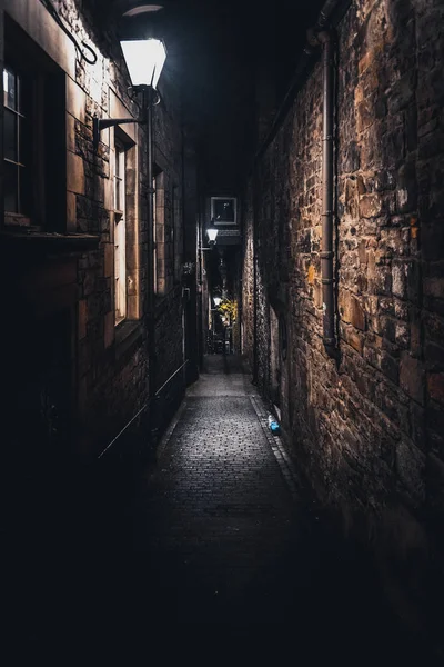 A dark creepy narrow European alley at night, surrounded by bricks and cobblestone. Illuminated only with some street lamps. Concept of scared or being alone and frightened — Stock Photo, Image