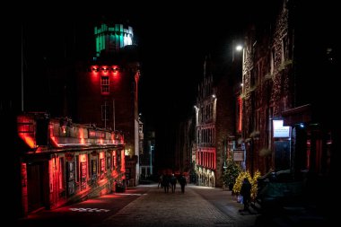Edinburgh, İskoçya 13 Aralık 2018: Geceleri Victoria Caddesi boyunca yürüyen insanlar renkli ışıklı binalarla çevrili. Sert ışık ve karanlığın karışımı.