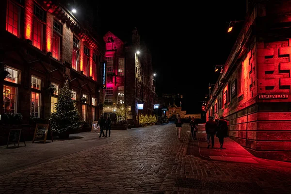 Edynburg, Szkocja 13 grudnia 2018: ludzie chodzą wzdłuż Victoria St. i Ramsay Lane, w nocy otoczony kolorowymi oświetlone budynki z zamkiem w tle. — Zdjęcie stockowe