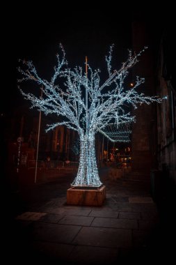 EDINBURGH, SCOTLAND 13 ARALIK 2018: İskelet çerçeveli şaşırtıcı bir ağaç heykeli, noel ışıkları parlıyor ve caddenin karanlığına doğru parlıyor.