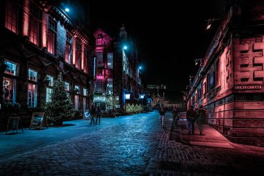 Edinburgh, İskoçya 13 Aralık 2018: Victoria St. ve Ramsay Lane boyunca yürüyen insanlar, geceleri arka planda kale ile renkli ışıklı binalarla çevrili.
