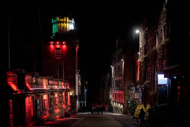 Edinburgh, İskoçya 13 Aralık 2018: Victoria St. gecesi renkli ışıklı binalarla çevrili bir gecede daire içinde toplanan insanlar. Sert ışık ve karanlığın karışımı.