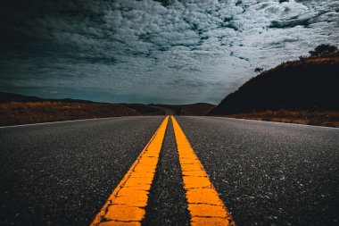 Eski asfalt yolda sarı şerit çizgileri ve yaz günü mavi gökyüzünde bulutlar.