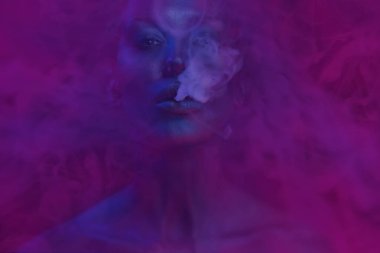 Kadın duman. Vape parti, gece hayatı. Güzel seksi genç kadınla duman exhaling gece kulübünde, göz alıcı mistik makyaj vaping. Kulüpte sigara kız. Mavi mistik duman