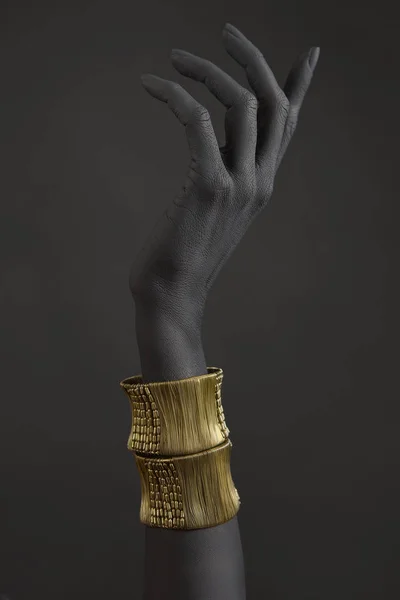 Black woman's hand with gold jewelry. Oriental Bracelets on a black painted hand. Gold Jewelry and luxury accessories on black background closeup. High Fashion art concept