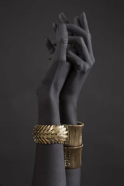 Black woman\'s hands with gold jewelry. Oriental Bracelets on a black painted hand. Gold Jewelry and luxury accessories on black background closeup. High Fashion art concept