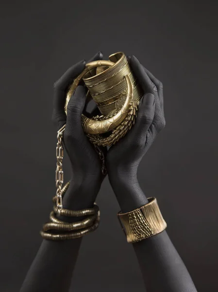 Black woman's hands with gold jewelry. Oriental Bracelets on a black painted hand. Gold Jewelry and luxury accessories on black background closeup. High Fashion art concept