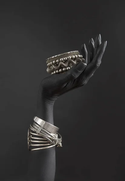 Black woman\'s hand with Silver jewelry. Oriental Bracelets on a black painted hand. Silver Jewelry and luxury accessories on black background closeup. High Fashion art concept