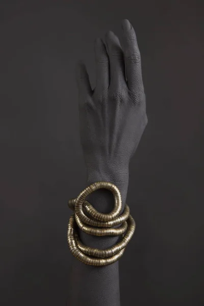Black woman's hands with gold jewelry. Oriental Bracelets on a black painted hand. Gold Jewelry and luxury accessories on black background closeup. High Fashion art concept
