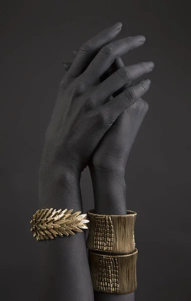 Black woman\'s hand with gold jewelry. Oriental Bracelets on a black painted hand. Gold Jewelry and luxury accessories on black background closeup. High Fashion art concept
