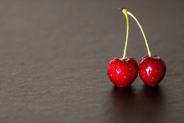 two red cherries with drippings on a black table