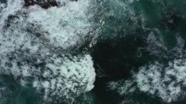 Devasa okyanus dalgalarının çarpışma ve köpürme görüntülerinin yukarıdan aşağıya doğru görüntüsü. Kamçatka, Pasifik Okyanusu. 4k video