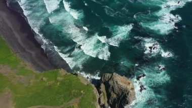 Okyanus mavi dalgalarının insansız hava aracının 4K görüntüsü kayalık bir dağın yüksek uçurumunda kırılıyor. Sahilde tehlikeli deniz dalgaları.