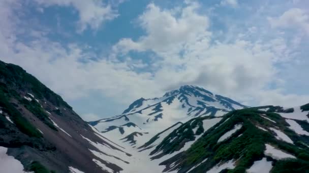 Timelapse en la cima de un volcán con una vista de las nubes que corren a través de las montañas. Los volcanes están cubiertos de abetos verdes y ocasionalmente nieve en un día nublado. Peínsula de Kamchatka — Vídeo de stock