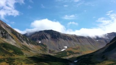Zirveleri, otlakları, renkli ormanları, Kamçatka yarımadası, 4k görüntüsü, dağlardaki bulutların aşırı hızlanması olan sonbahar dağının üzerinden insansız hava aracı uçuşu.