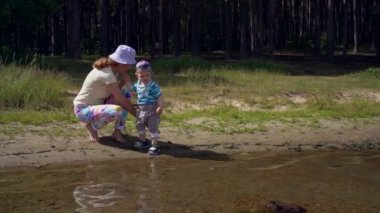 Anne ve küçük oğlu bir orman gölünün kıyısında su kenarında çakıl taşları ile oynamak. Anne ve bebeği bu yaz hafta sonu birlikte.