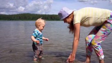 Anne ve küçük oğlu oynamak ve mavi bir gökyüzüne karşı güneşli bir yaz gününde bir orman gölünün berrak su etrafında sıçrama