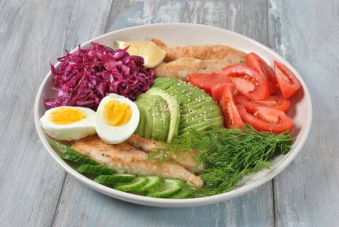 Tavuk salata avokado, domates, kırmızı lahana, salatalık, haşlanmış yumurta ve maydanoz ile. Ahşap arka plan sağlıklı gıda kavramı üzerinde tavuk ve sebze ile sağlıklı öğle yemeği kase