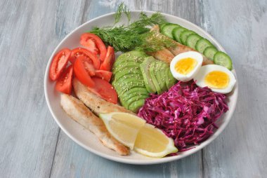 Tavuk salata avokado, domates, kırmızı lahana, salatalık, haşlanmış yumurta ve maydanoz ile. Ahşap arka plan sağlıklı gıda kavramı üzerinde tavuk ve sebze ile sağlıklı öğle yemeği kase