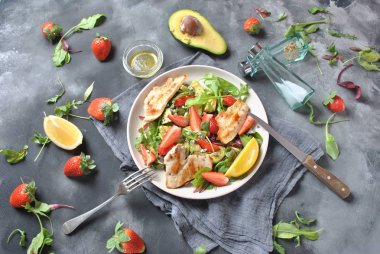 Tavuk avokado, çilek, mavi peynir, roka salatası, pancar yaprakları. Sağlıklı yemek avokado kase, tavuk ve koyu gri arka plan üzerinde çilek ile plaka. Sağlıklı gıda kavramı