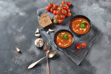 Sıcak kış çorbası. Sarımsak, tatlı kırmızı biber, maydanoz, gri bir arka plan üzerinde iki siyah seramik kase krem ve hamur mayası ekmek ile servis ile kırmızı sıcak domates çorbası 