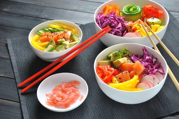 Poke bowls with fresh salmon, crystal noodles, radish, avocado, sweet pepper, cucumber, sesame seeds, red cabbage. Organic food. Fresh seafood recipe. Food concept poke bowl on wooden background