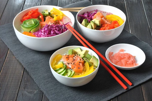 Poke bowls with fresh salmon, crystal noodles, radish, avocado, sweet pepper, cucumber, sesame seeds, red cabbage. Organic food. Fresh seafood recipe. Food concept poke bowl on wooden background