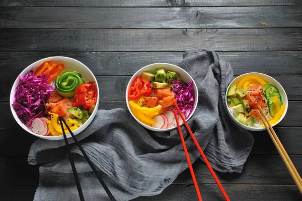 Poke bowls with fresh salmon, crystal noodles, radish, avocado, sweet pepper, cucumber, sesame seeds, red cabbage. Organic food. Fresh seafood recipe. Food concept poke bowl on wooden background