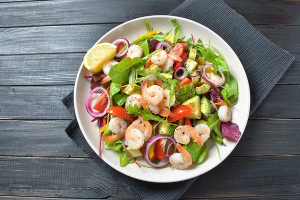 Avocado salad with shrimps, cherry tomatoes, arugula beet leaves, red onion, yellow sweet pepper. Healthy lunch plate with vegetables and shrimps